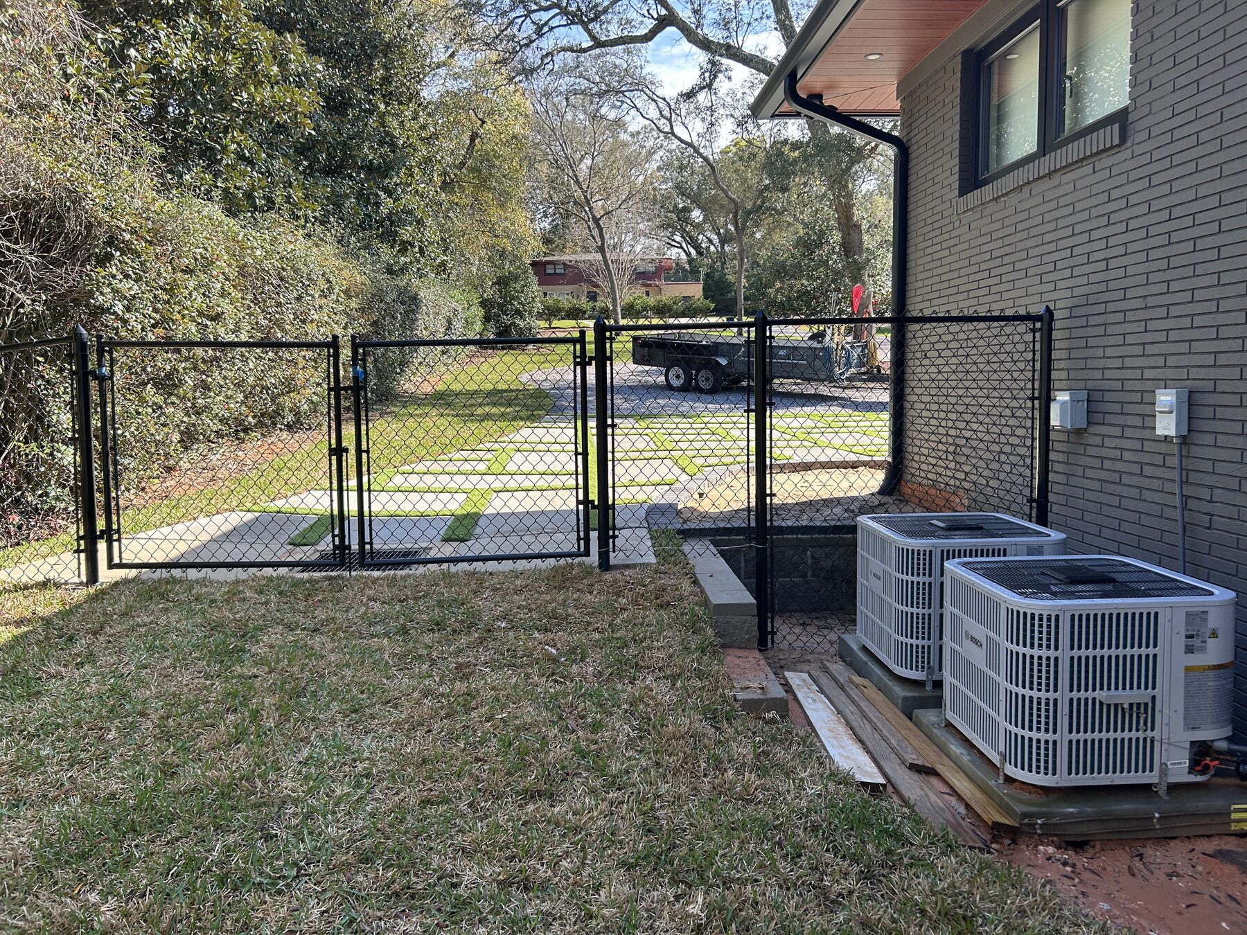 Black chain link fence with two gates enclosing a side yard and HVAC units
